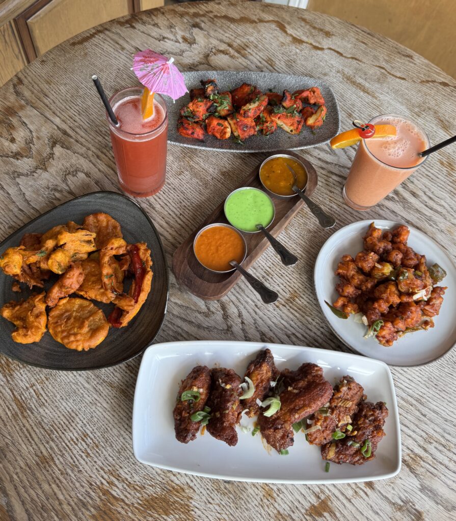 Indian appetizer feast with vegetable pakoras, chicken tikka, wings, and chutneys at Cinnamon Lounge.