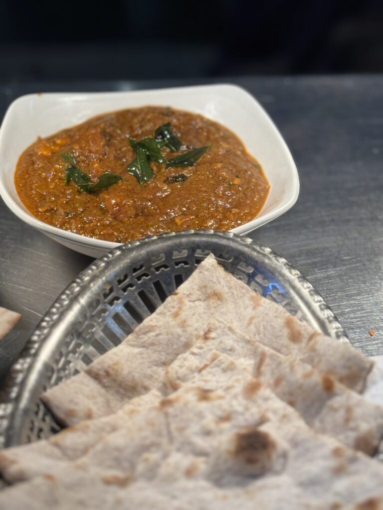 Traditional Indian curry served with fresh naan flatbread on a silver platter at Cinnamon Lounge.