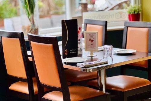 A dining table set with wooden, orange-upholstered chairs, plates, glasses, and standing wine menus in a brightly lit restaurant (2)